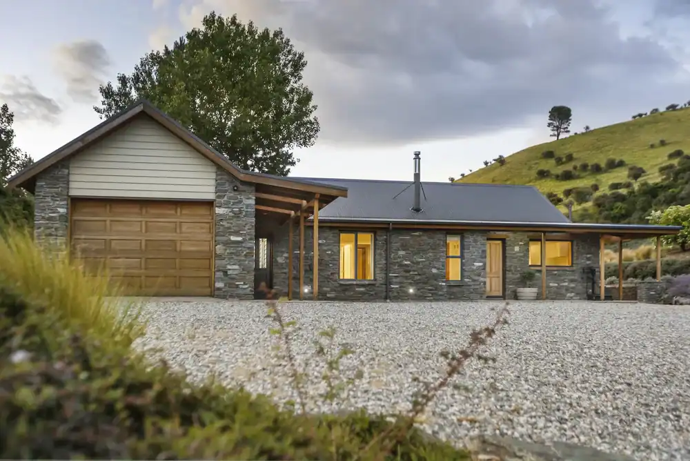 Charming stone cottage with metal roof at Judge & Jury Village, surrounded by lush greenery and scenic mountain views, offering a peaceful retreat experience.