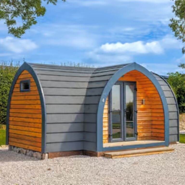 Judge & Jury Village mountain cabin in alpine scenery, surrounded by tall pine trees and a flowing creek, representing a rustic, natural setting for outdoor adventure and wilderness experiences.